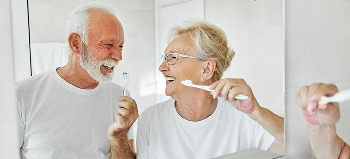 Senior couple smiling while brushing their teeth