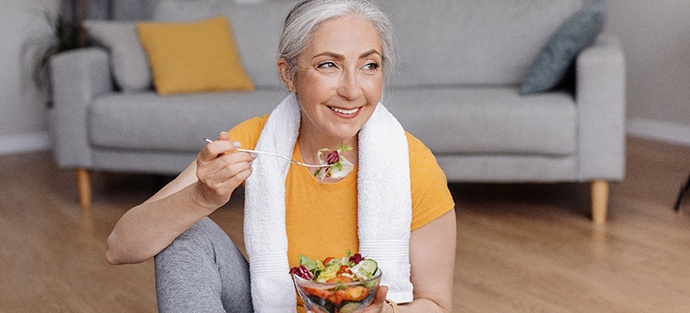 Senior woman smiling while eating salad at home